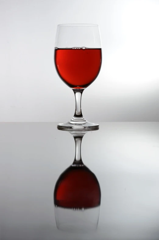 red liquid in a wine glass reflecting its reflection on a gray background