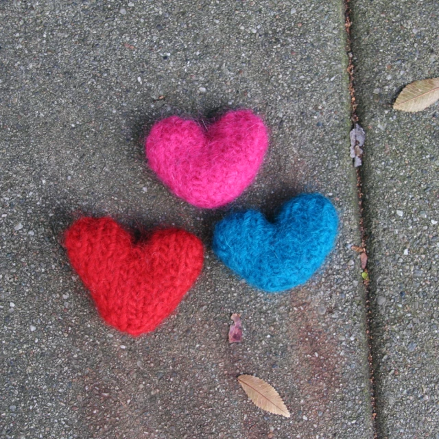 two knitted hearts sitting on the ground, one blue and one pink