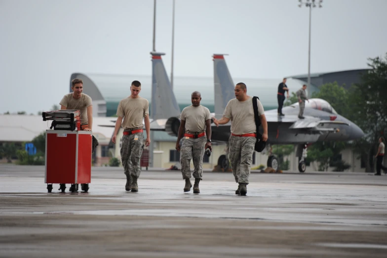 four men wearing military uniform holding luggage walking on concrete