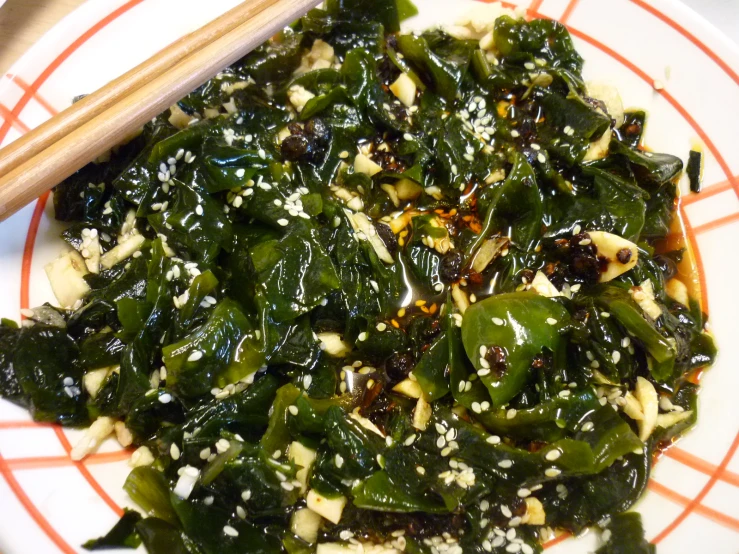 a bowl filled with spinach and spices next to a pair of chopsticks