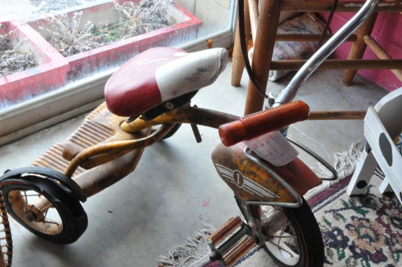 an old tricycle is near a window and rugs