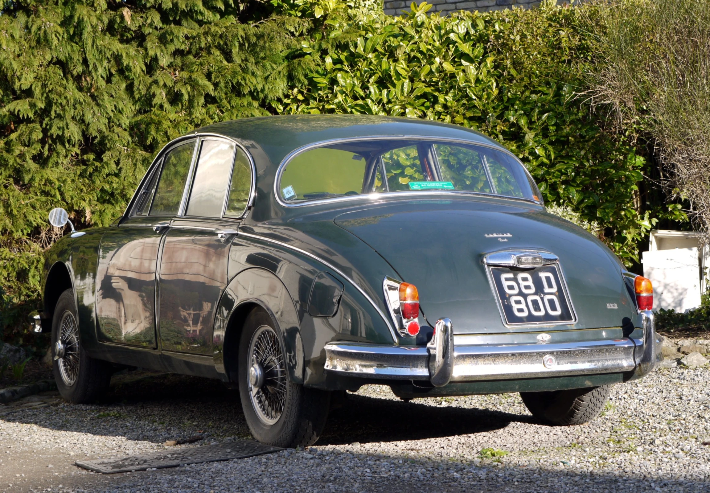 an old grey car is parked next to a hedge