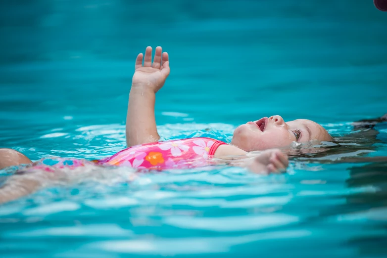 a little girl laying down in the pool with an orange frisbee