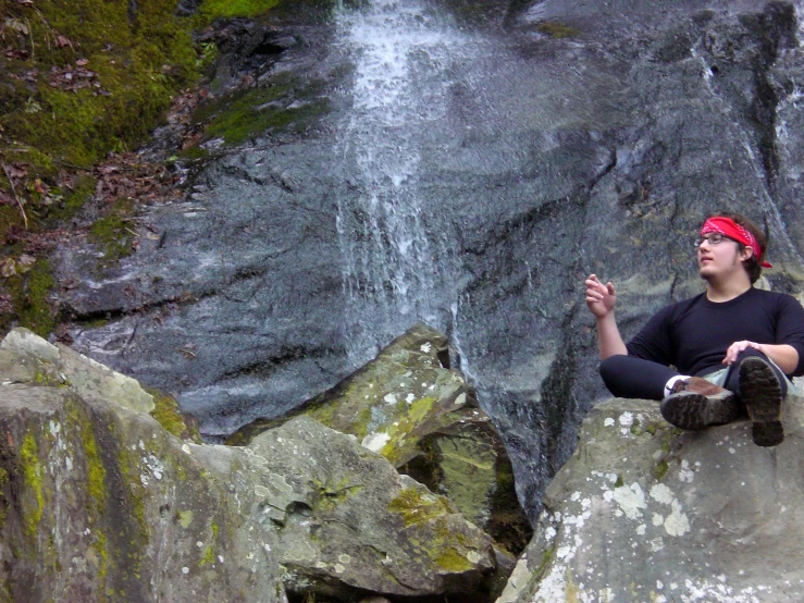 a man sitting on top of a large rock next to a waterfall