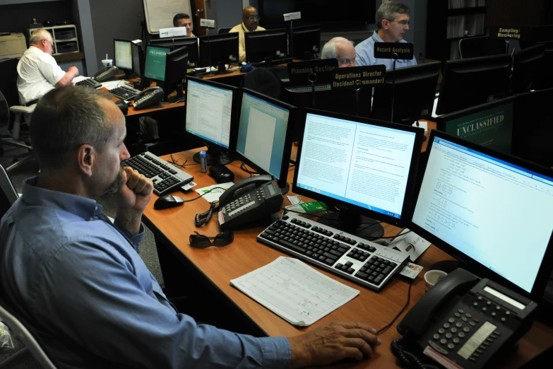 two men work at a desk surrounded by multiple computers