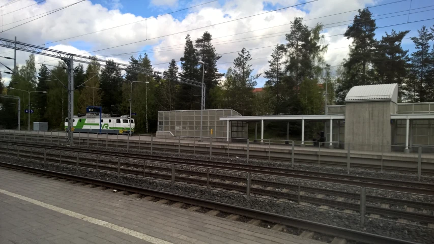 a green train is at a station under some trees
