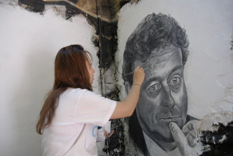 woman painting a picture of the actor john mellennan on a wall