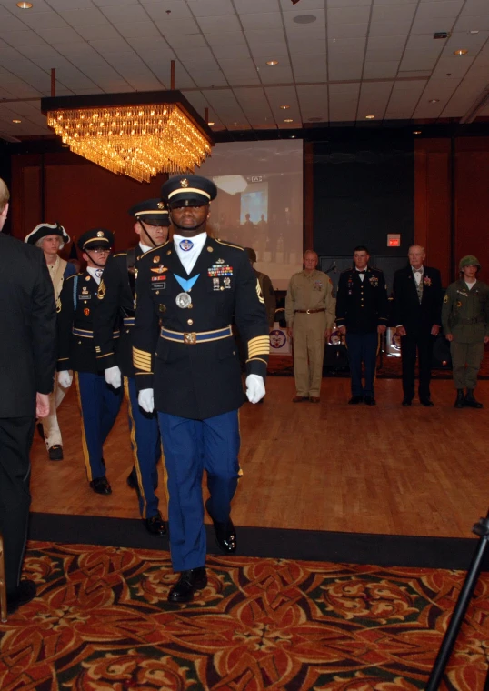 several uniformed personnel walk on a brown carpet with people in formal wear