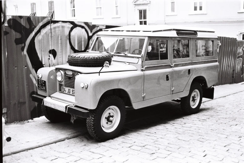 the defender is parked beside a wall with graffiti