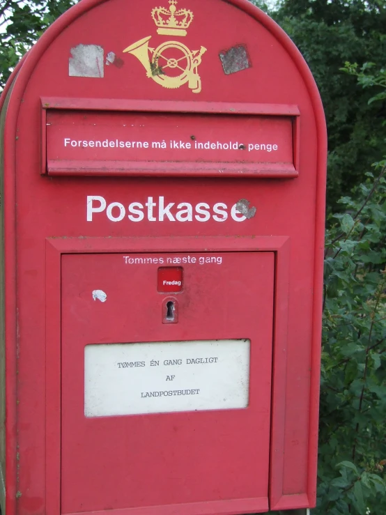 red mailbox with stamps out front, sitting beside a bush