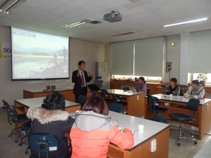 several people are sitting and standing around a classroom