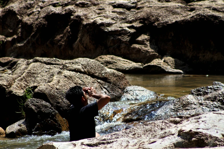 a man stands in some water near a rocky cliff