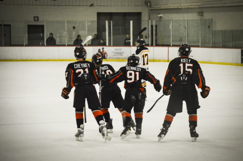 five players in black and orange uniforms playing hockey