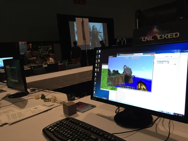 several monitors on a computer desk and people in the background