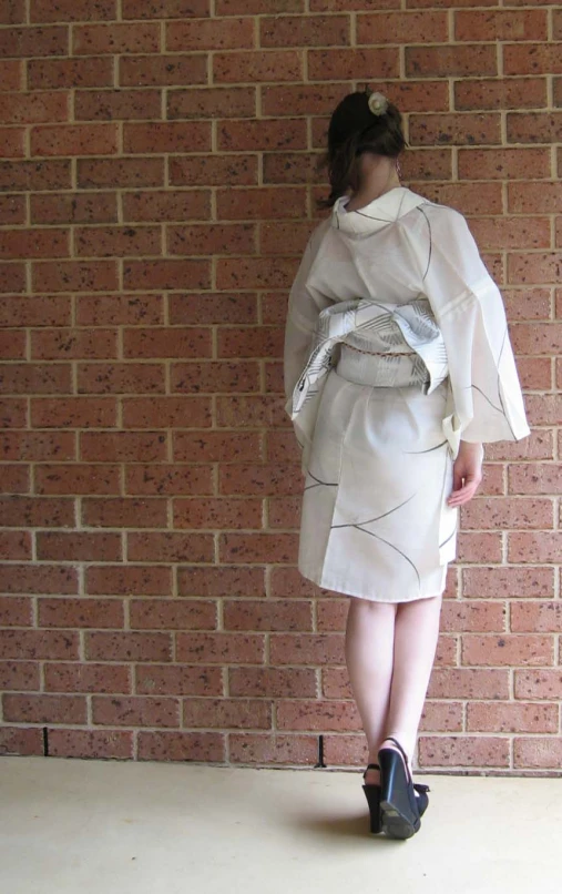 a woman dressed in white is by a brick wall