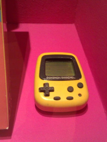 an old yellow electronic game on display on a pink surface