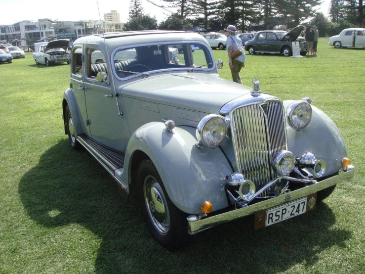 an older model car parked on the grass with some people in the background