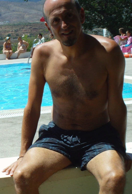 a bald man sitting on a surf board next to a swimming pool