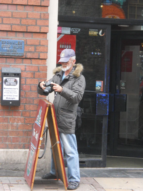 man on sidewalk with camera and sign in hand