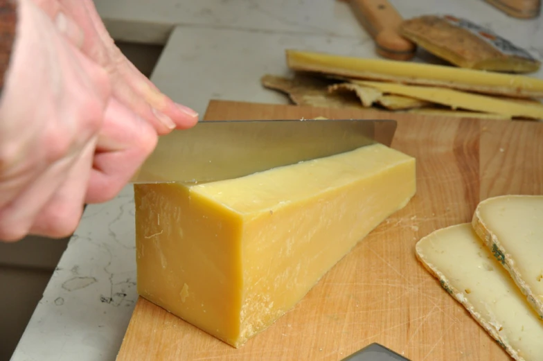 someone cuts cheese off of a wooden block