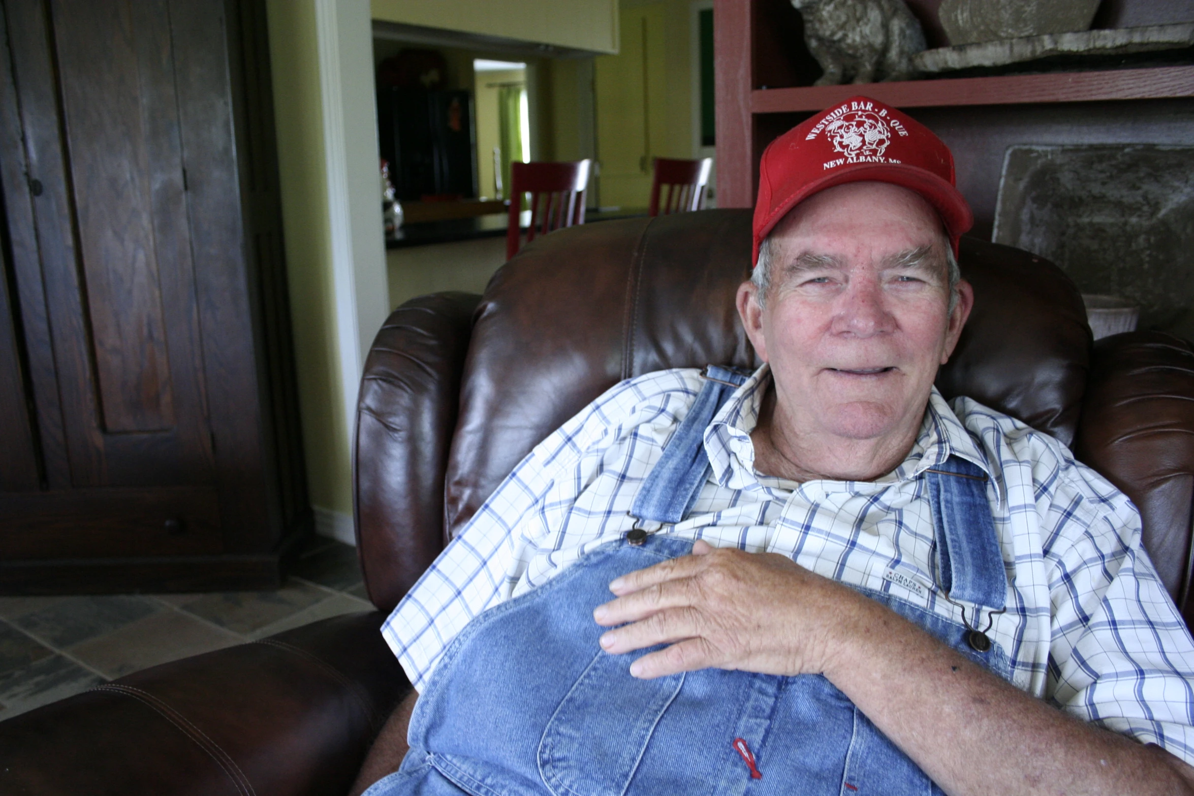 an older man wearing a red hat and overalls holds a cigar