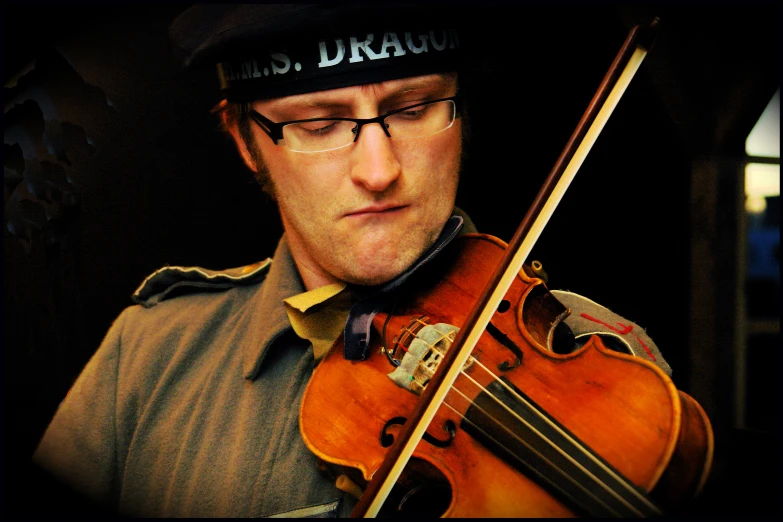 a man wearing glasses and a hat holding onto a violin