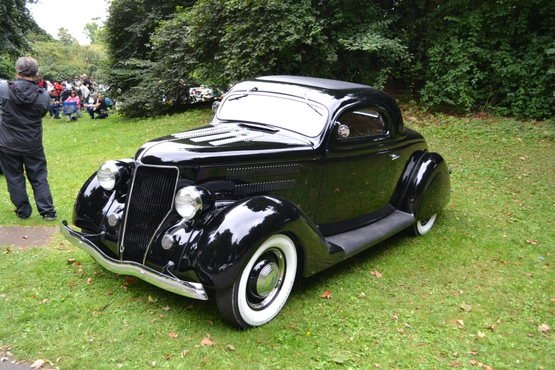 an old black car parked on top of a lush green field