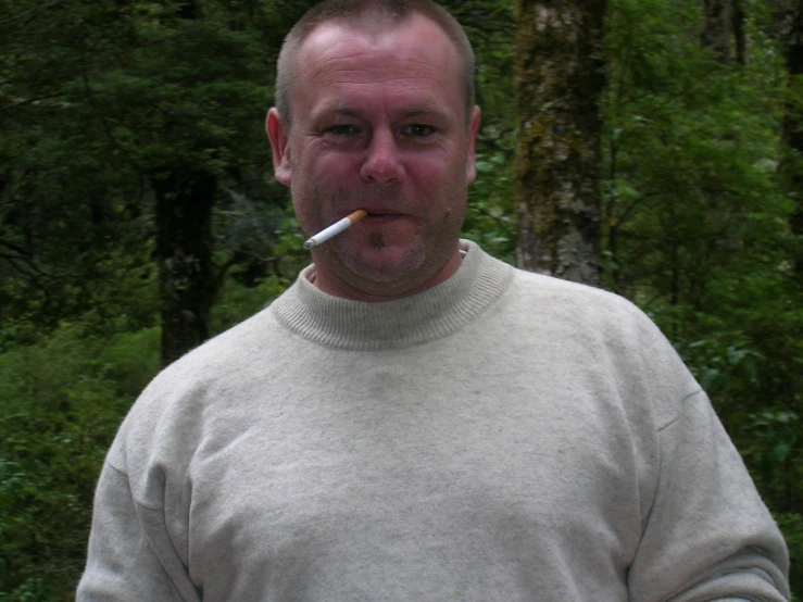 a man smoking a cigarette while standing in the woods