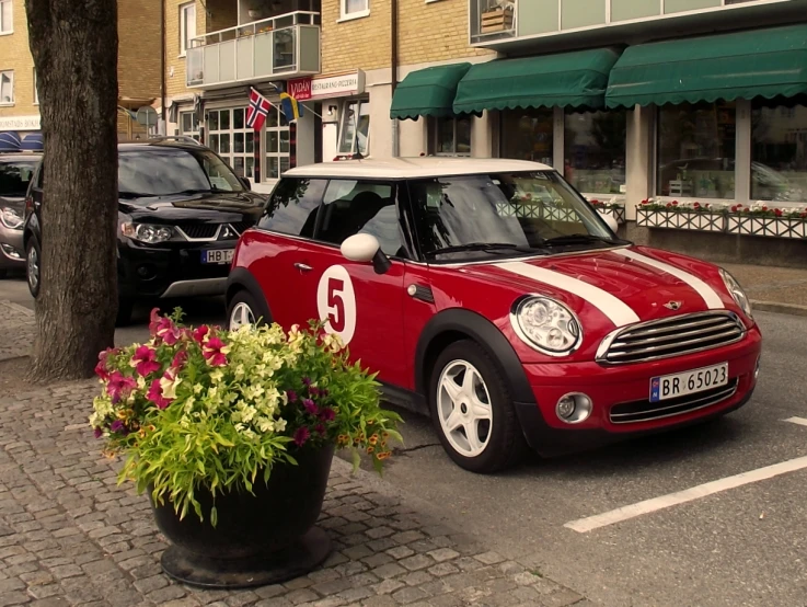 small, red car on a city street with colorful flowers