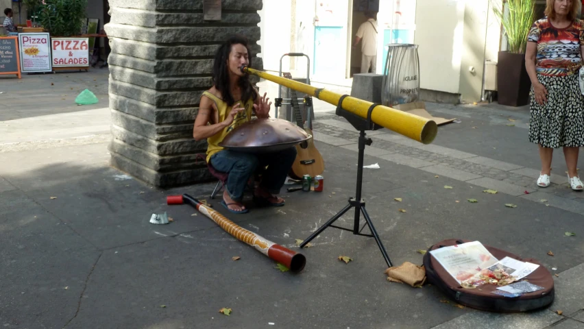 a girl sitting by a giant telescope on the street