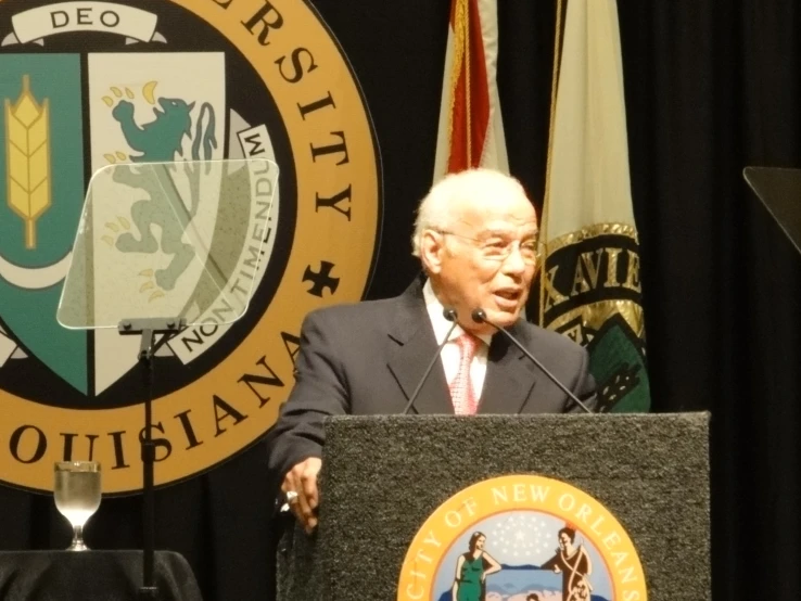 the man is speaking in front of the flag and emblem