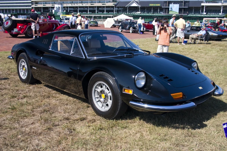 a black sports car sits in the grass next to people