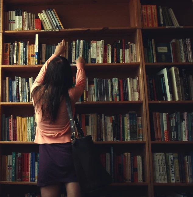 a girl in a pink shirt is holding onto books on a book case