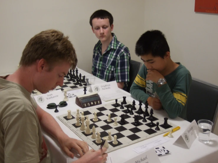 four boys sitting at a table playing chess