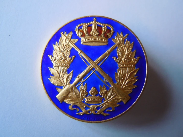 a blue and gold colored lapel pin with an image of a crown