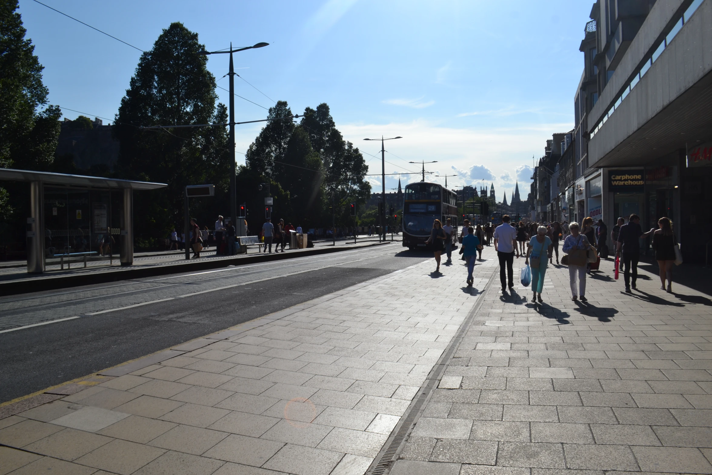 people walk down a sidewalk on a sunny day