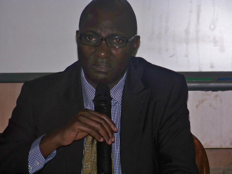 a black man in a suit sits in front of a microphone