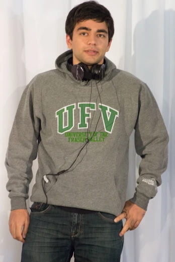 a man wearing a gray hoodie stands with headphones