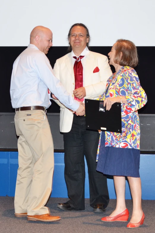 a man shakes the hands of two woman, while they are holding a lap top in each hand