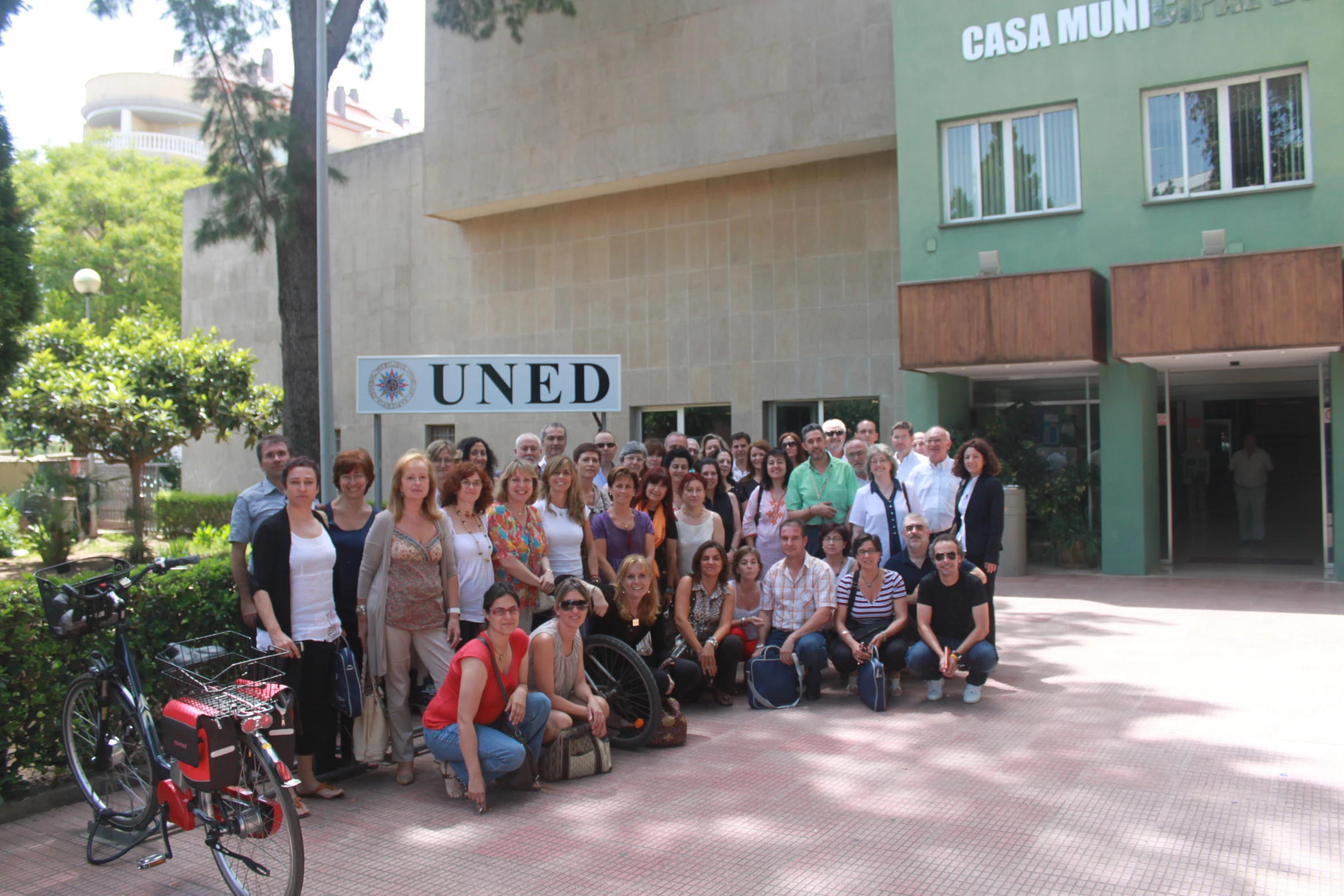 a group of people pose together with a bicycle near a building