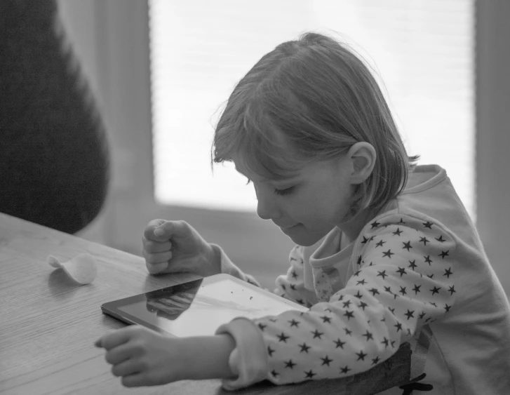 small girl holding a tablet while sitting at a table