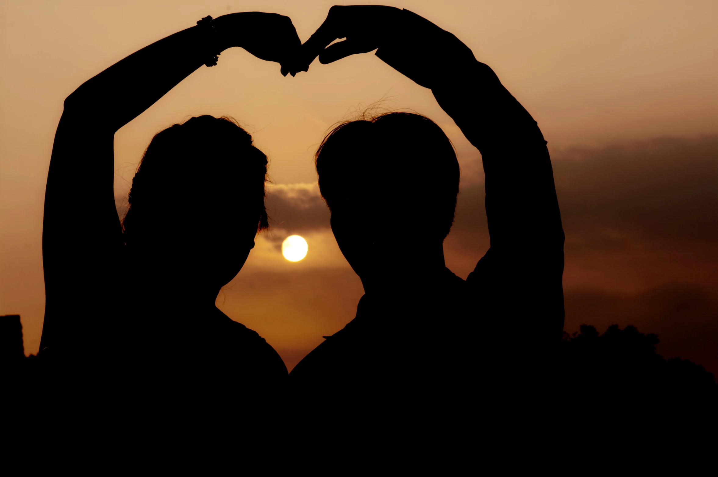 the silhouette of two people holding their hands in front of a sunset