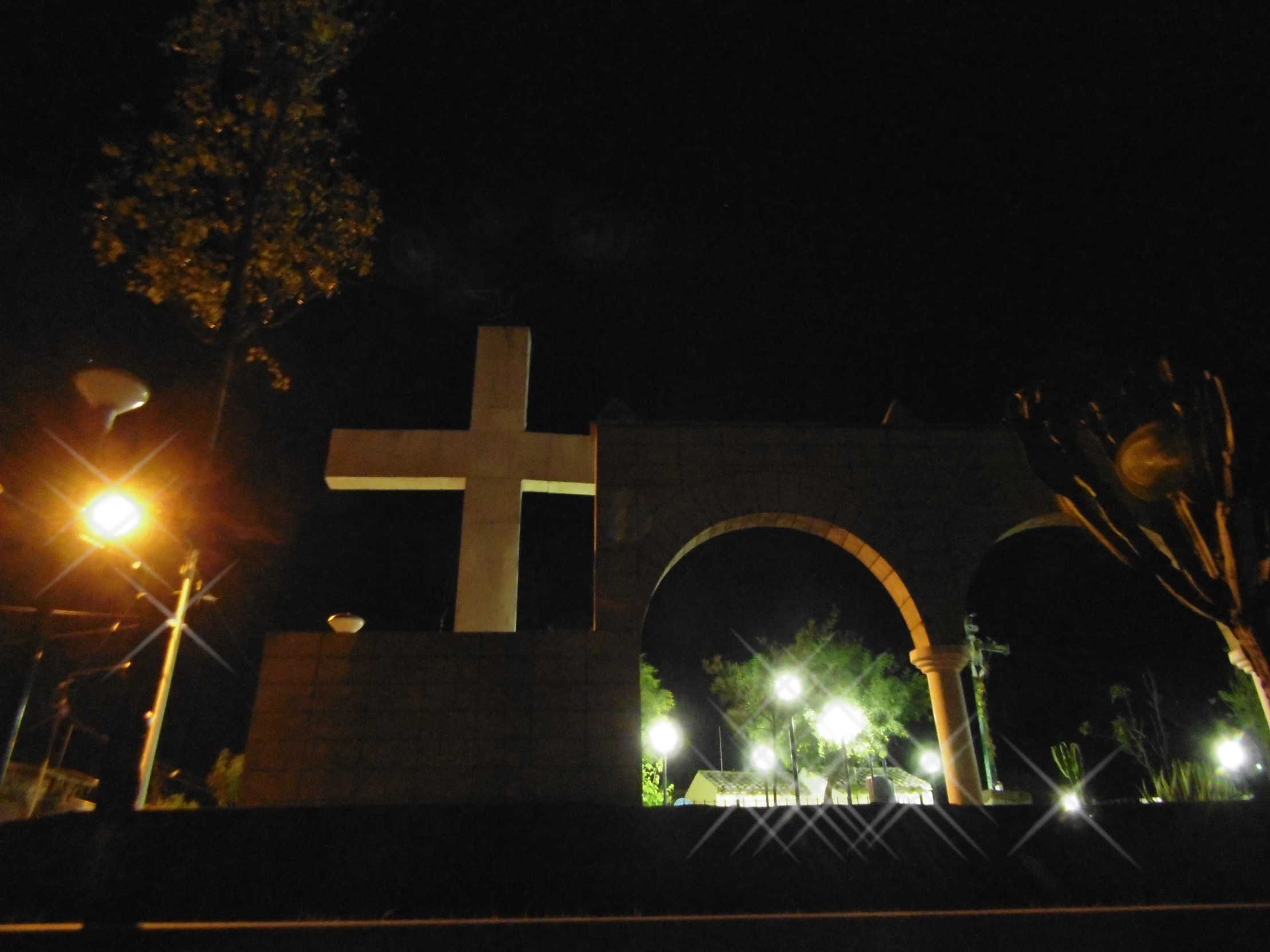 a cross stands next to a street lamp and fence