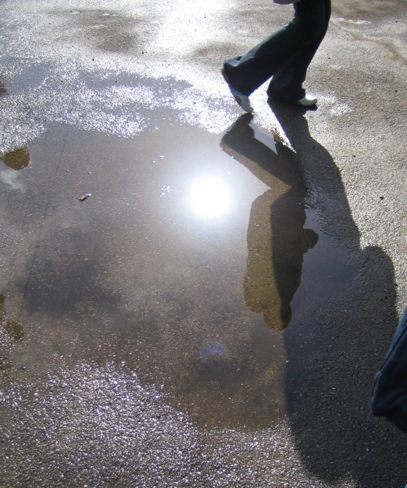 a reflection of someone in the street on a wet pavement