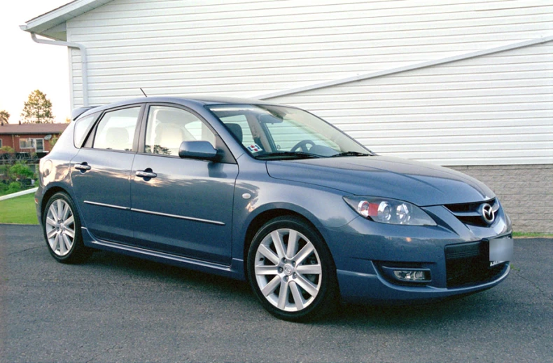 a gray car is parked on a street with buildings behind it