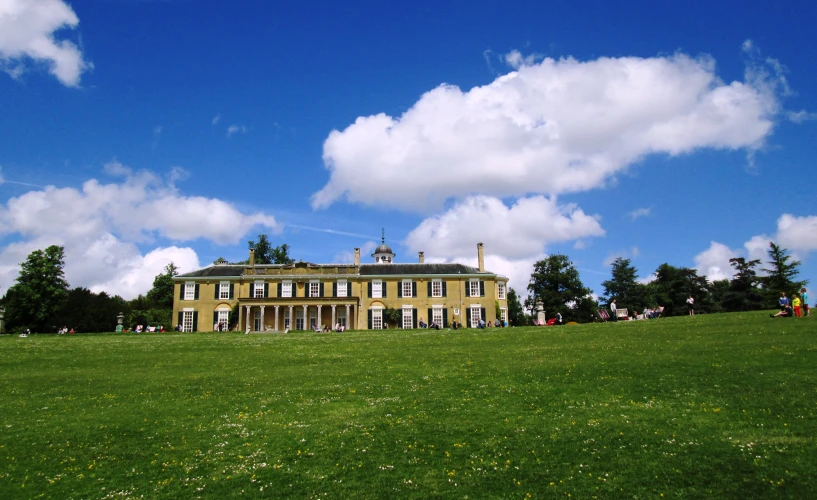 a huge mansion sits on a green grassy hill