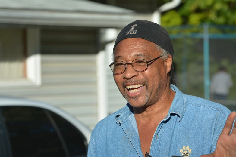 a black man with glasses smiling in front of a house