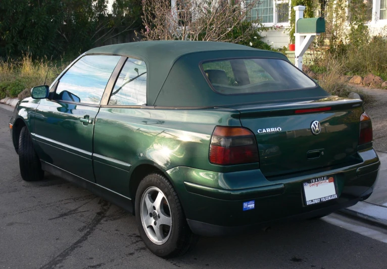 a green car sits parked on the curb next to an empty road