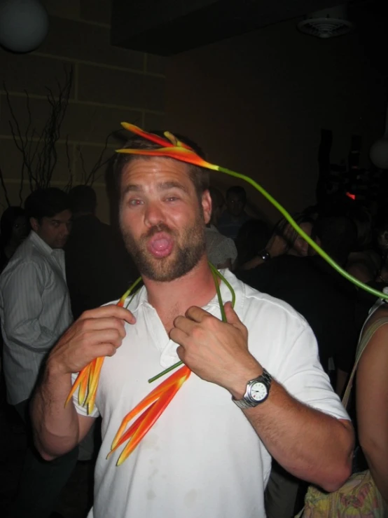 a man in a white shirt holds on to two colorful cords that look like feathers