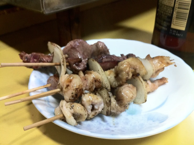 several skewered food items on white plate next to beer